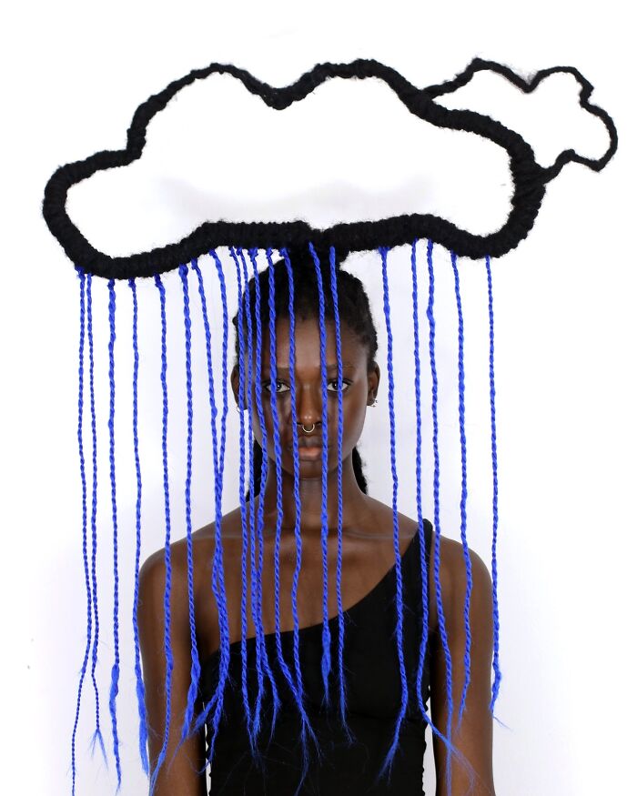 Artist with hair sculpture resembling cloud and rain, featuring blue braided strands and creative hairstyle design.