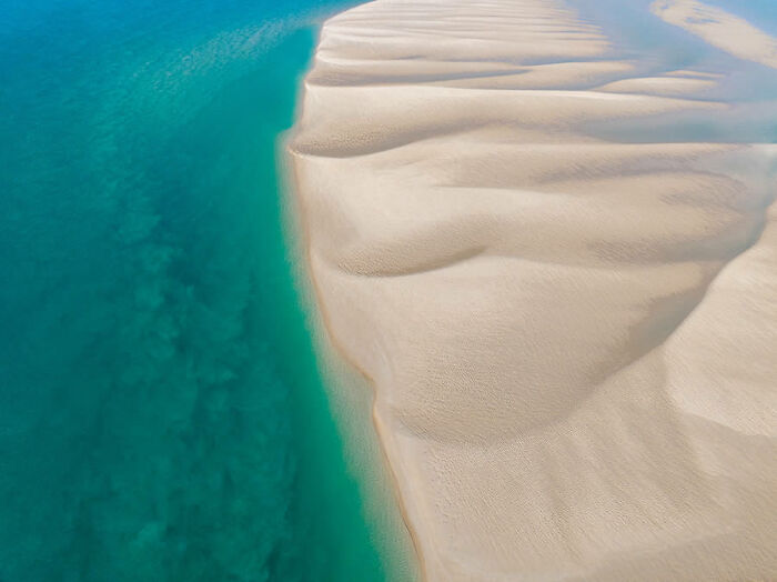 Aerial view of pristine sand dunes meeting turquoise ocean, showcasing breathtaking nature photography.