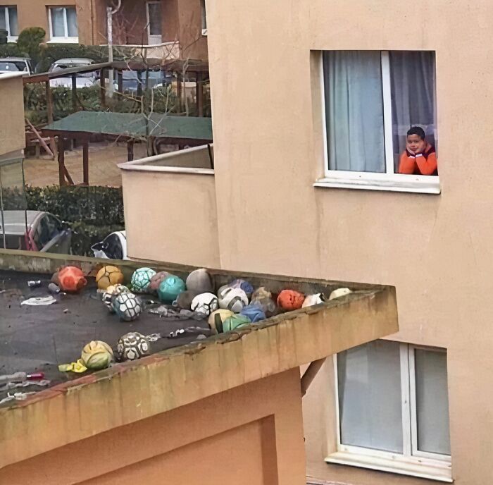 Child looking out a window at rooftop filled with various soccer balls, a quirky scene from a weird Instagram account.