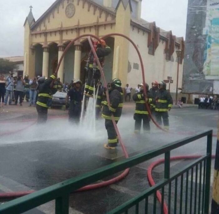 Firefighters holding a suspended hose, creating an arc of water; a bizarre scene from a strange Instagram account.