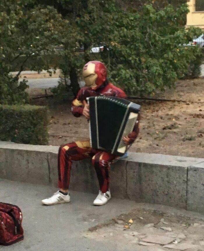 Person in superhero costume playing an accordion on a park bench, showcasing the weirdness of Instagram content.