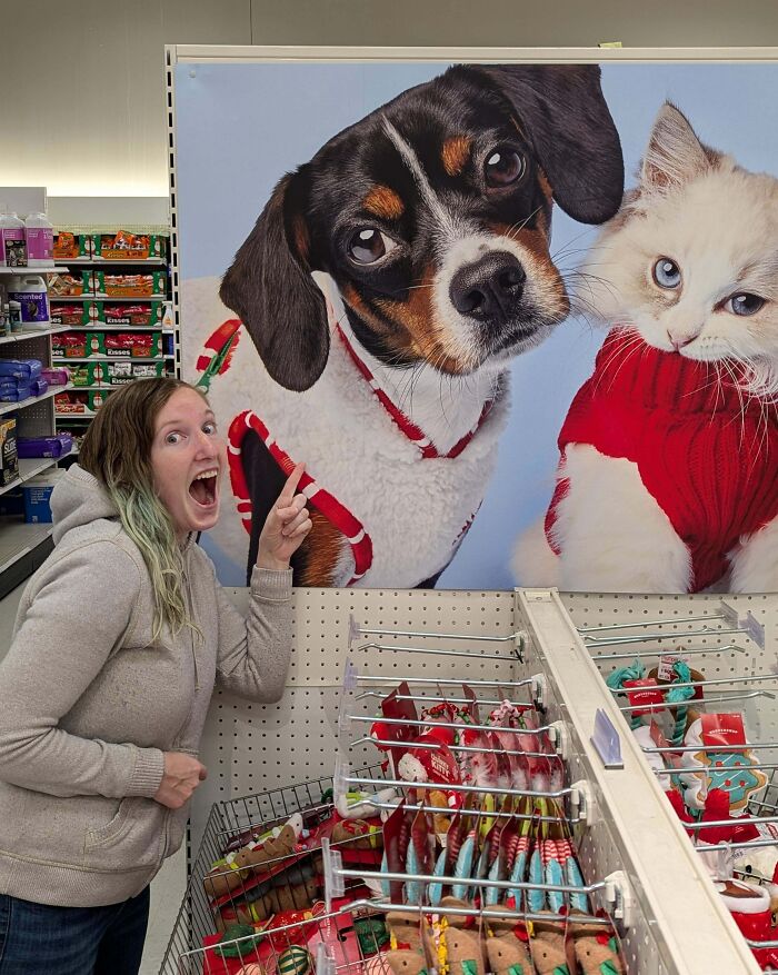 Mujer emocionada señalando imagen grande de perro y gato con suéteres, transmitiendo momentos positivos y conmovedores.