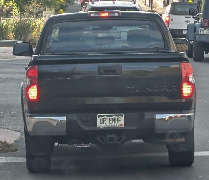 Black pickup truck with personalized Colorado license plate UR ENUF, a pure and uplifting moment on a city street.
