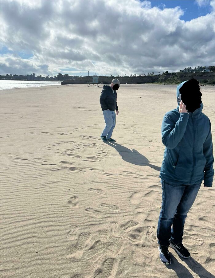 Two people wearing jackets walking on a sandy beach under a cloudy sky, capturing pure and uplifting moments.