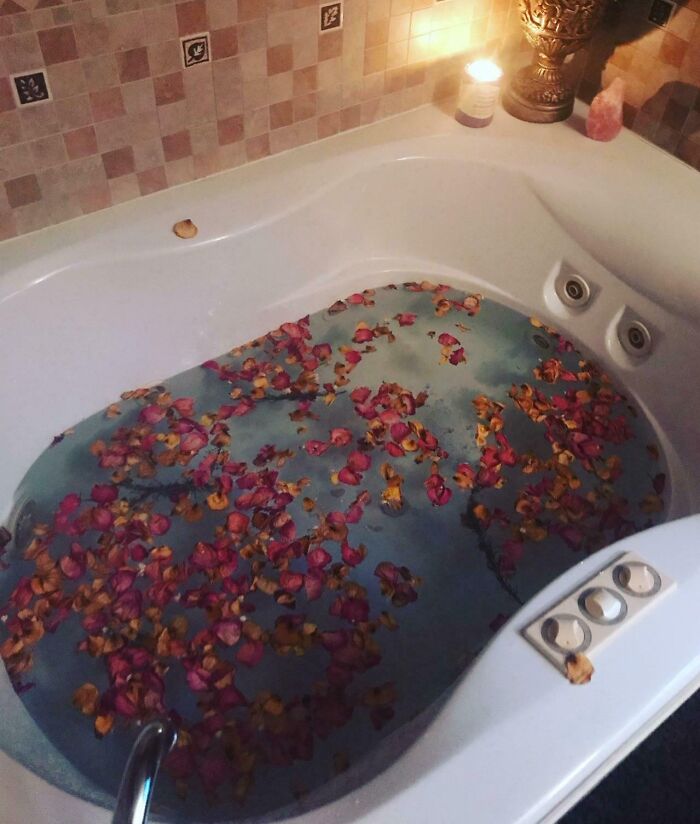 Bathtub filled with water and scattered rose petals, creating a pure and uplifting moment for daily relaxation.