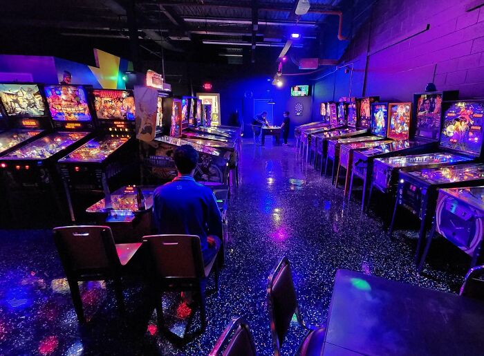 Sala de juegos con máquinas de pinball iluminadas y personas disfrutando momentos positivos y conmovedores.