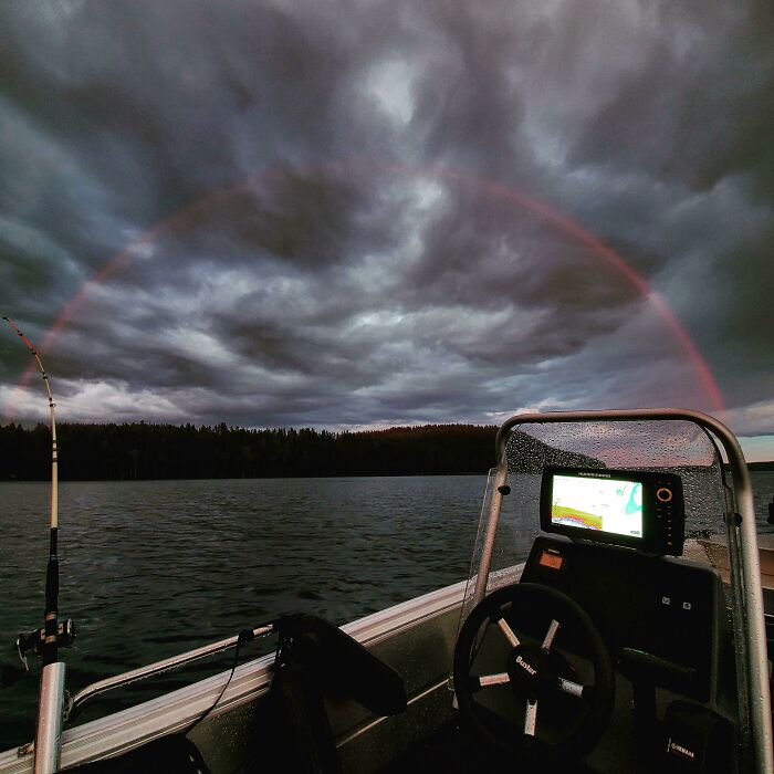 Fishing boat on a lake under a dark cloudy sky with a faint rainbow, showcasing one-in-a-million coincidences in nature.
