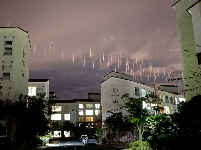 Night sky displaying unusual light streaks above residential buildings, a rare one-in-a-million coincidence captured.