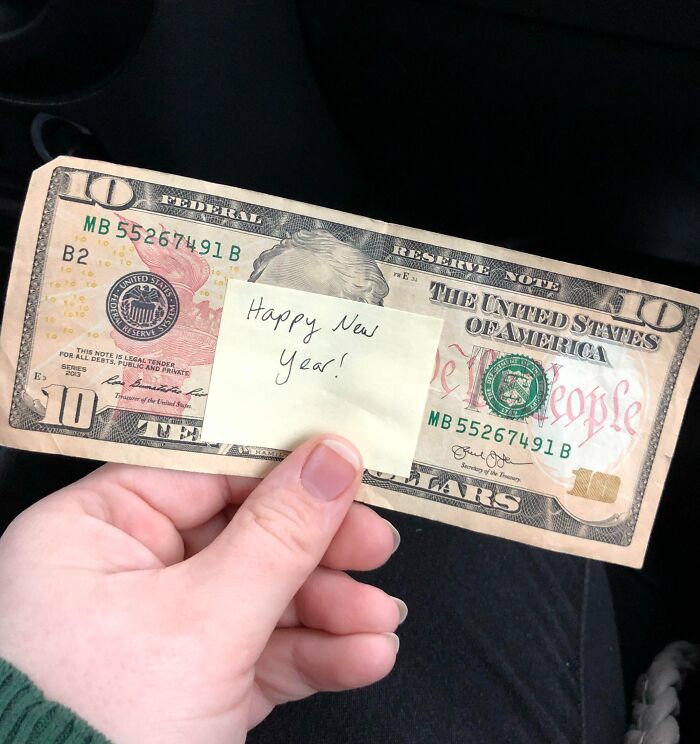 Hand holding a ten-dollar bill with a sticky note reading Happy New Year, a pure and uplifting moment.