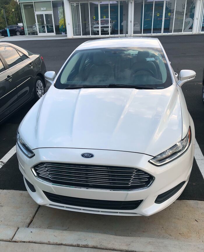 Auto Ford blanco estacionado frente a edificio, mostrando momentos positivos y conmovedores para recobrar la fe en la humanidad.