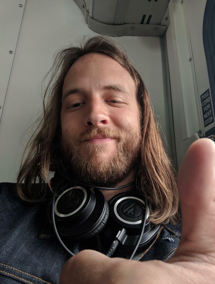 Hombre sonriente con audífonos alrededor del cuello mostrando un pulgar arriba, momentos positivos y conmovedores humanidad.