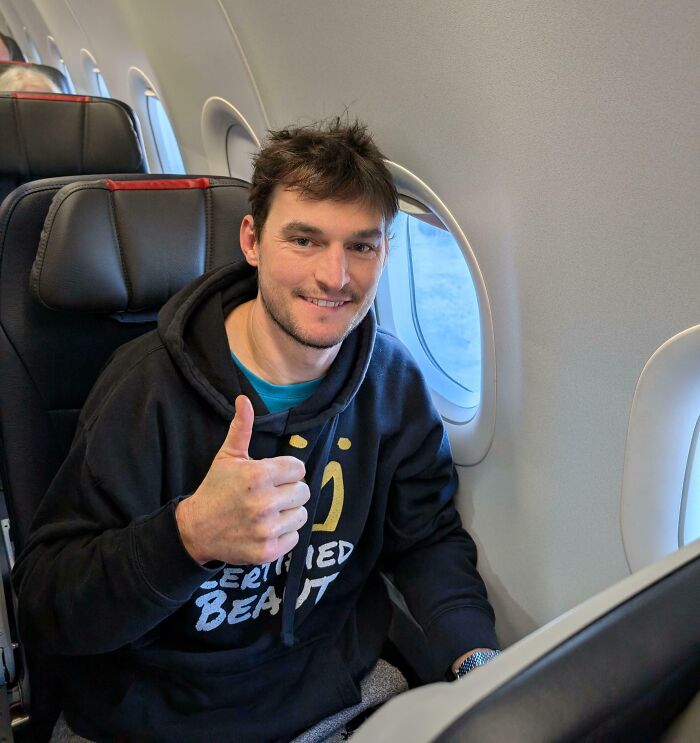Man smiling and giving thumbs up on airplane seat, capturing pure and uplifting moments during daily scroll.