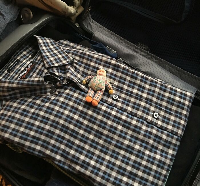 Camisa a cuadros doblada en maleta con muñeco de tela encima, simbolizando momentos positivos y conmovedores en la humanidad.