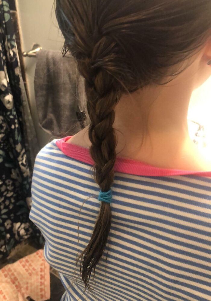 Close-up of a simple braid in dark hair with a blue hair tie, capturing a pure and uplifting daily moment in casual attire.