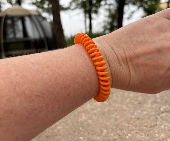 Orange spiral hair tie worn on wrist as a time saver tool for quick access outdoors with blurred background.