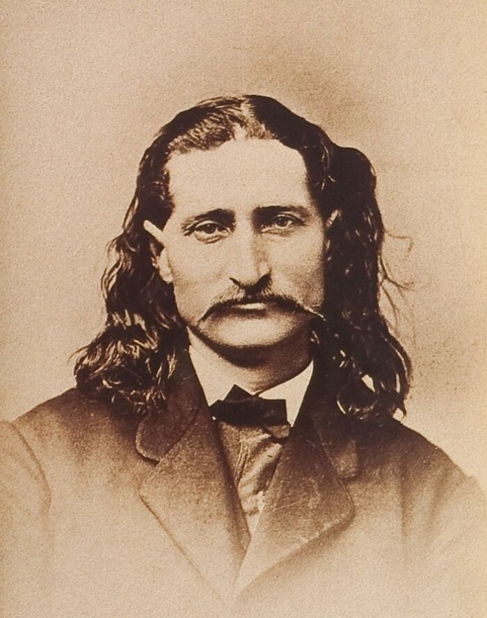 Sepia tone rare photo of a famous historical figure with long hair and a mustache wearing a suit and bow tie.