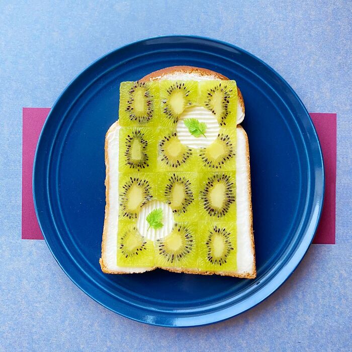 Creative toast design with kiwi slices arranged on bread, displayed on a blue plate.
