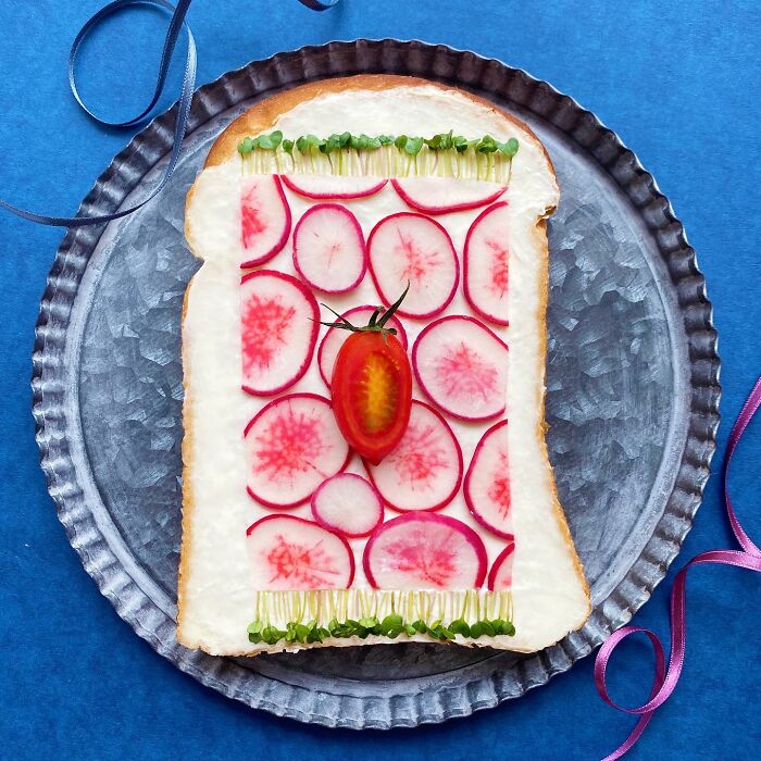 Creative toast design with radish slices and cherry tomato on a metal plate.
