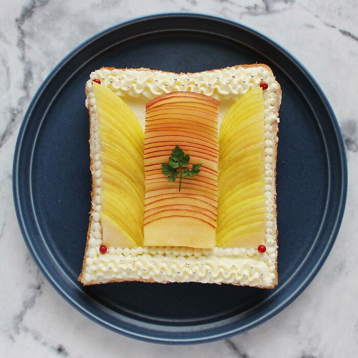 Creative toast design with sliced apples and a parsley garnish on a blue plate.