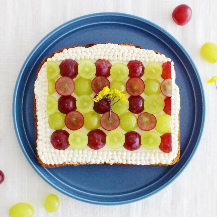 Creative toast design featuring grapes and cream by Japanese artist, displayed on a blue plate.