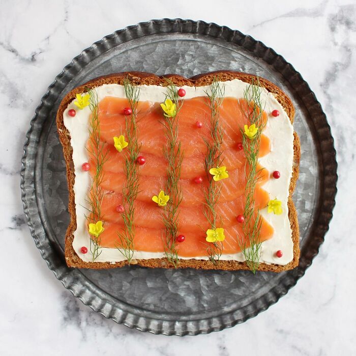 Creative toast design with salmon, dill, and yellow flowers on a metal plate.