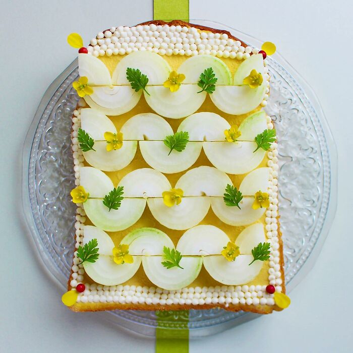 Creative toast design by Japanese artist featuring intricate decorations with herbs and vegetables on a glass plate.