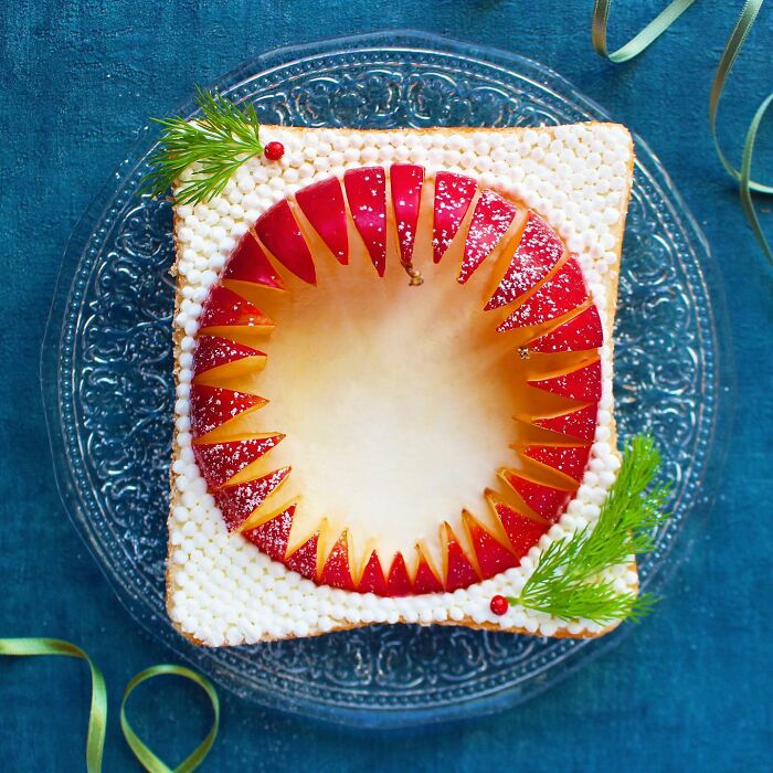 Creative toast design featuring intricate red and white apple cutouts on a square slice, presented elegantly on a clear plate.