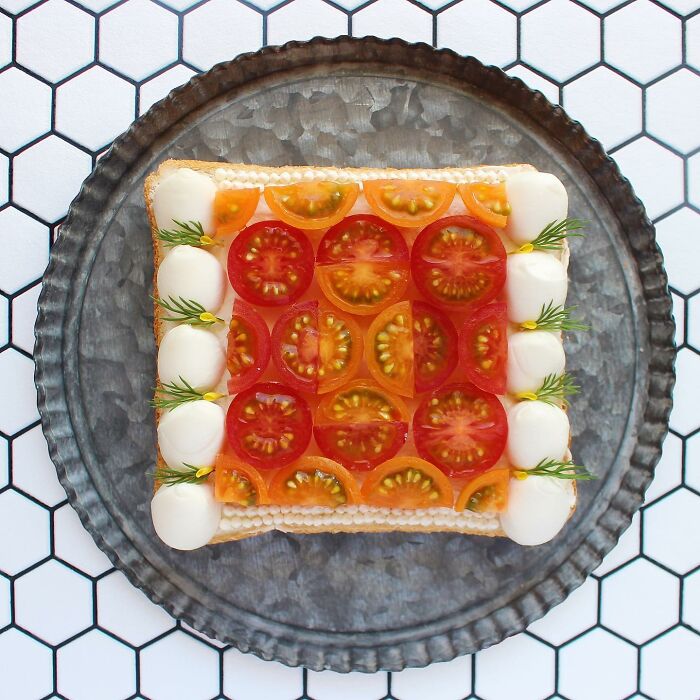 Creative toast design with colorful tomatoes and herbs on a patterned tray.