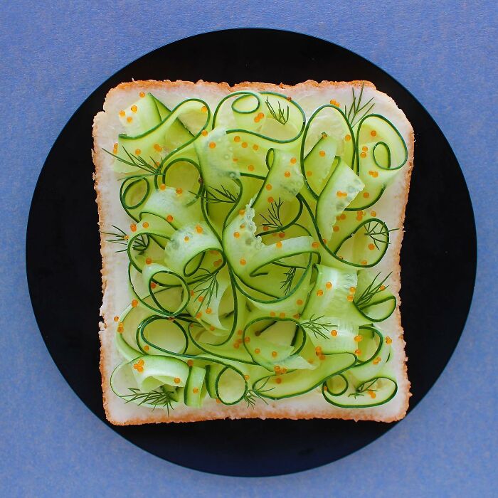 Creative toast design featuring intricate cucumber ribbons and herbs on a plate.