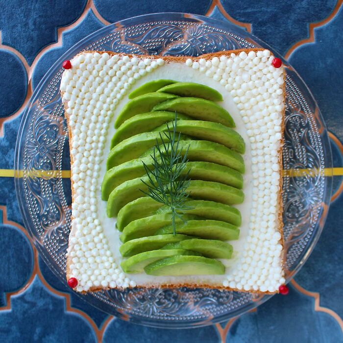Creative toast design with avocado slices and dill on patterned plate.