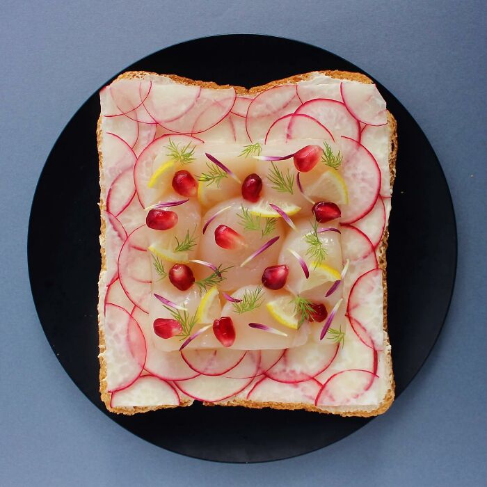 Creative toast design featuring radish slices, pomegranate seeds, lemon wedges, and dill arranged artistically on a black plate.