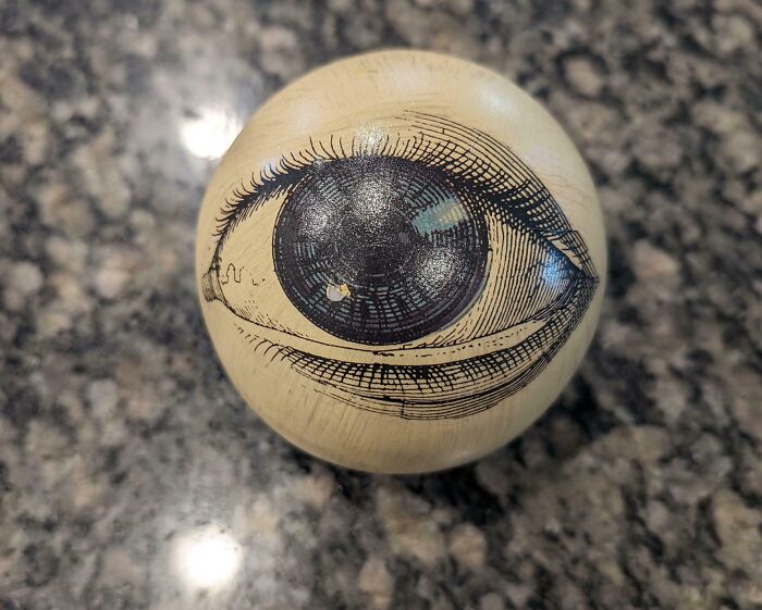 A marble ball with an eye illustration, a unique Goodwill find on a speckled surface.