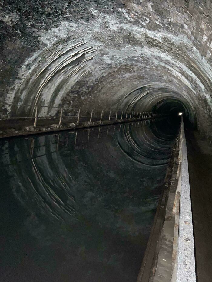 Dark creepy underground tunnel with reflective water and arched stone ceiling creating eerie atmosphere.