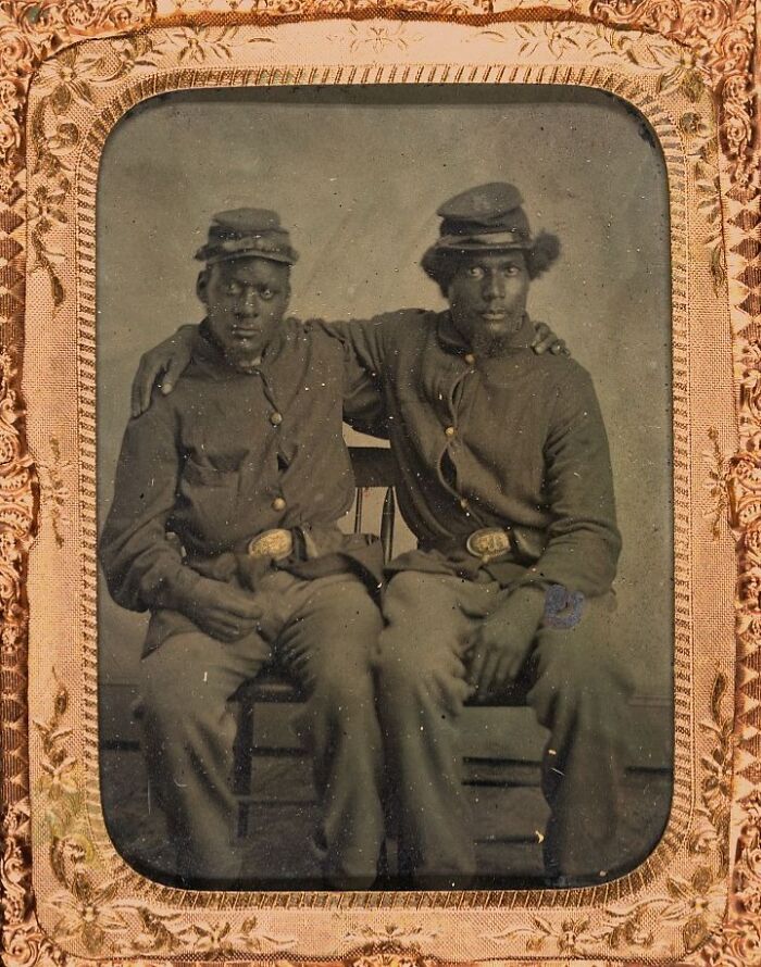 Two African American soldiers from over a century ago sitting and posing together, showcasing strength and unity.