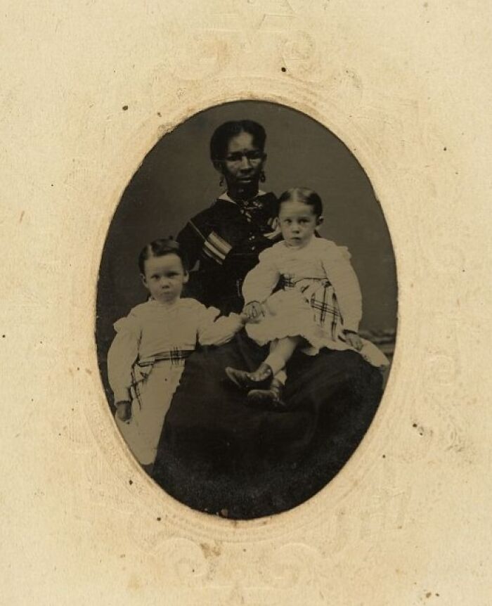 African American woman showing strength, dressed in vintage clothing, holding two young children in historic photo.