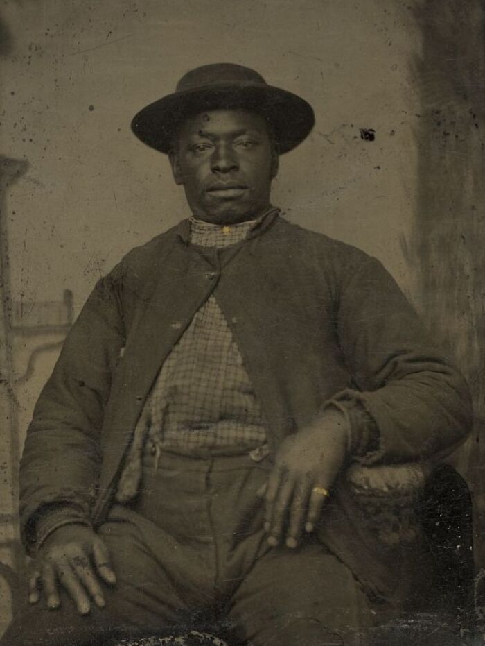 African American man from over a century ago seated, wearing a hat and jacket, showing strength and resilience in history.