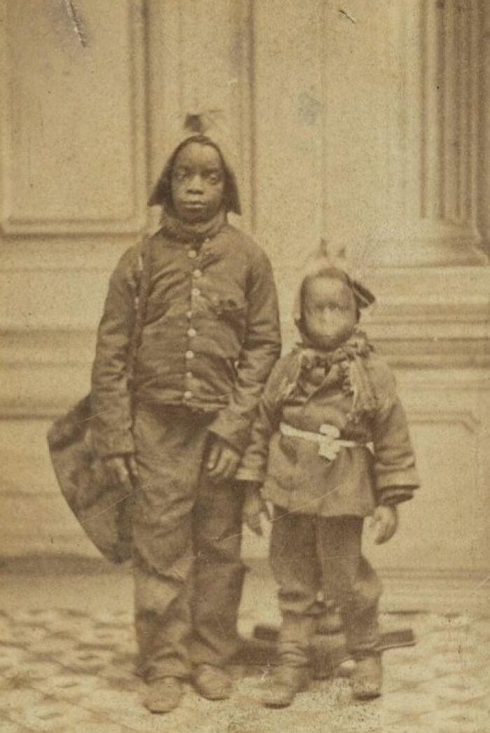 Two African American boys dressed in historical clothing, standing strong in a powerful early photo over a century ago.