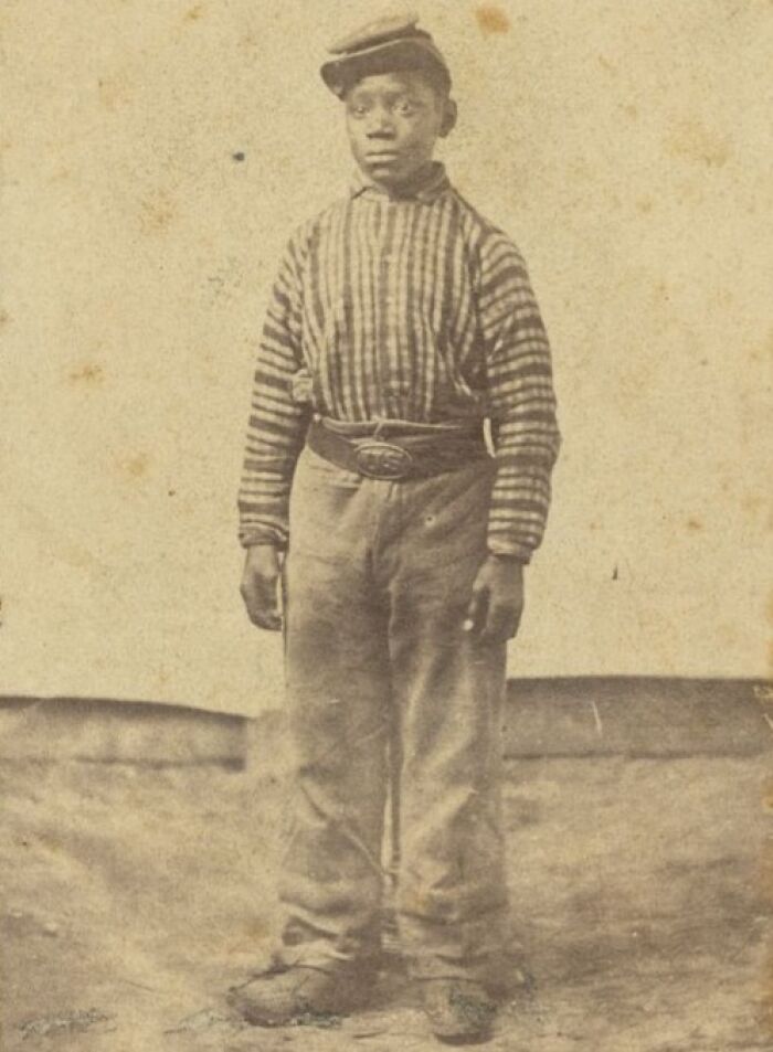 Young African American boy standing in striped shirt and cap, symbolizing strength in historic powerful photos over a century ago.