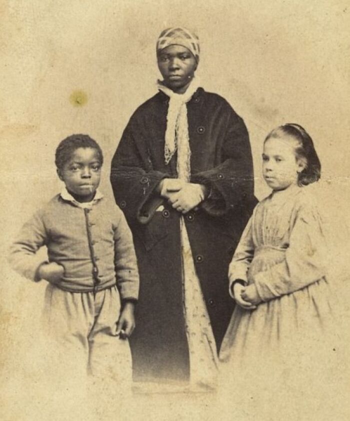 African American woman and two children in vintage clothing, showcasing strength in a powerful historical photo over a century ago.