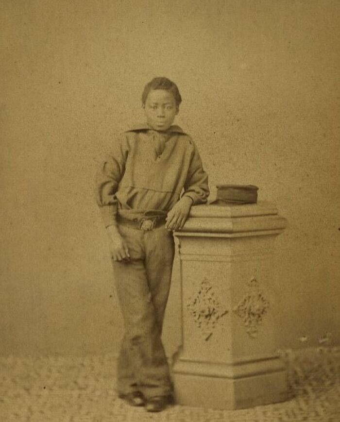 Young African American boy from over a century ago leaning on a decorative pedestal, showcasing strength and resilience.