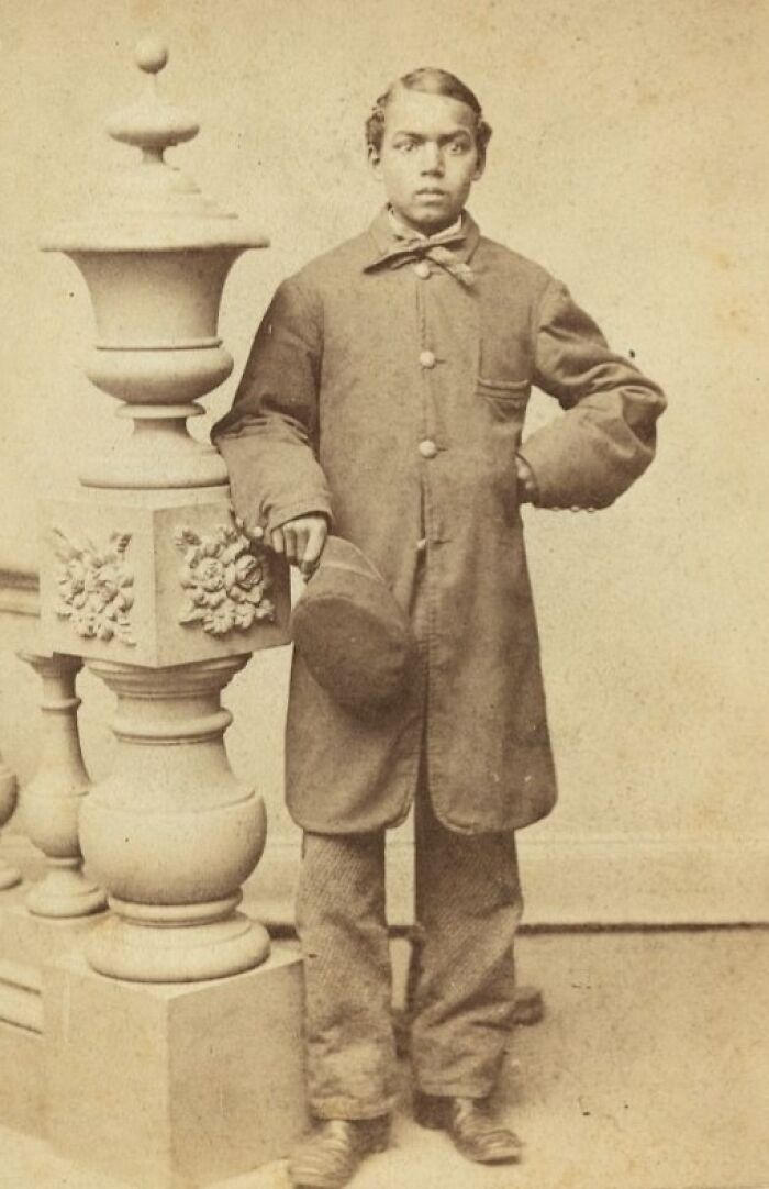 Young African American man from a century ago standing confidently by an ornate stone pillar, embodying strength and resilience.