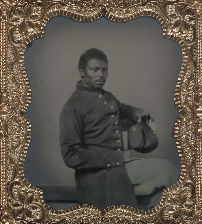 African American man in historic military uniform holding cap, showcasing strength in a powerful century-old photo.
