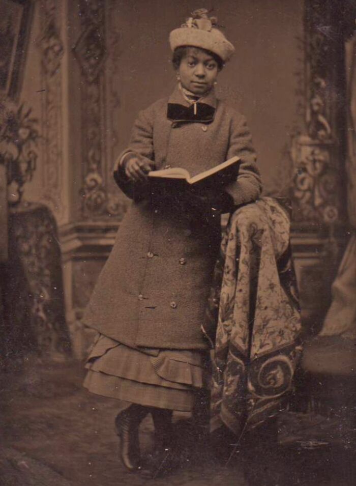 African American woman from over a century ago dressed formally, holding a book, symbolizing strength and resilience.