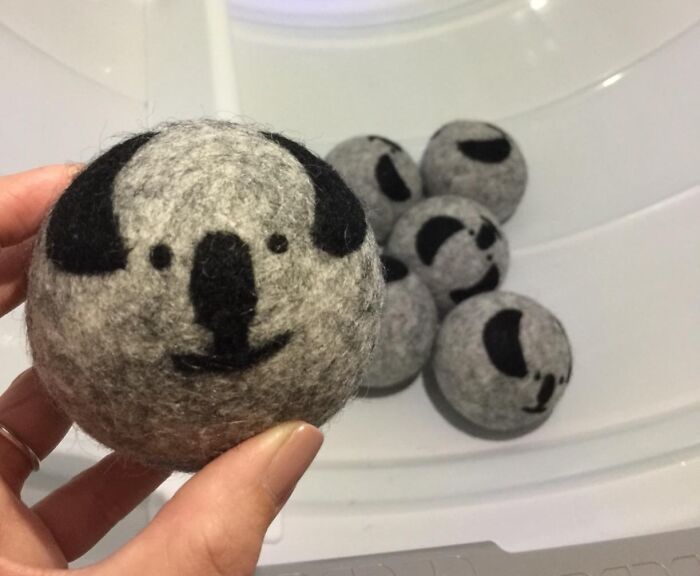 Hand holding a felt ball with a cute koala face, with more similar felt balls in the background, bright and cheerful.