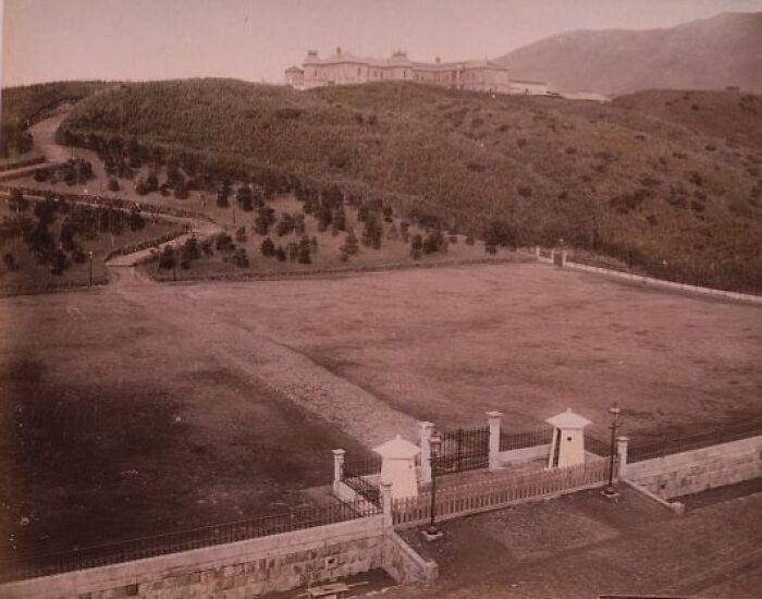 Historic landscape of Japan in the 1800s featuring a large estate on a hill with surrounding greenery and pathways.