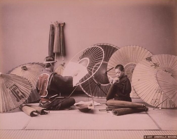 Japanese umbrella makers crafting traditional umbrellas indoors, showcasing historical Japan look in the 1800s with authentic tools.