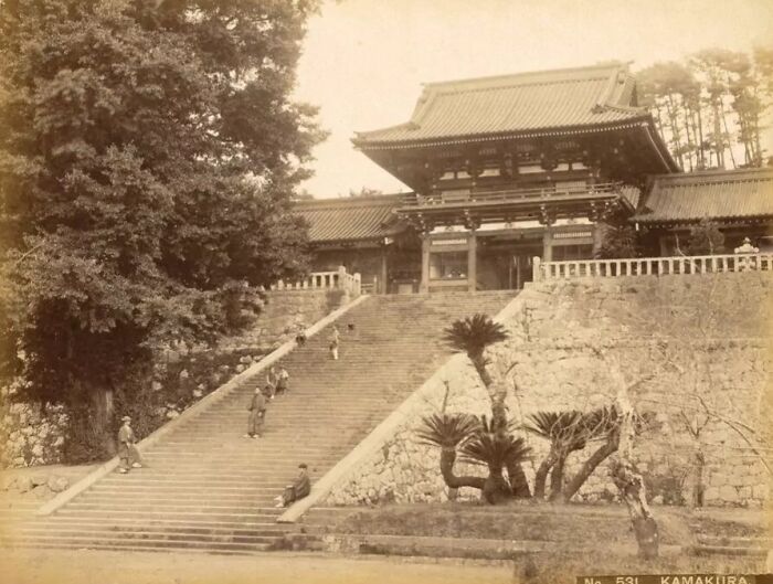 Historical sepia photo of traditional Japanese architecture and stone steps with people, showing Japan in the 1800s.