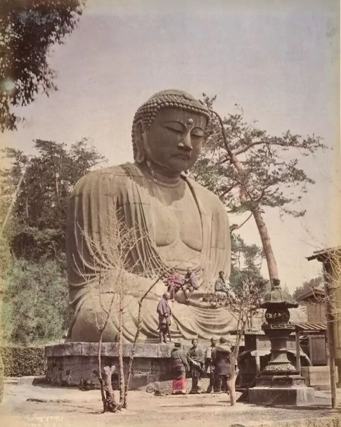 Large Buddha statue with people around it in historical Japan scene from the 1800s, surrounded by trees and traditional structures.