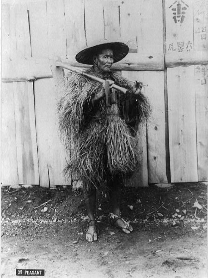 Japanese peasant in traditional straw raincoat and hat holding farming tool in 1800s Japan historical photo.