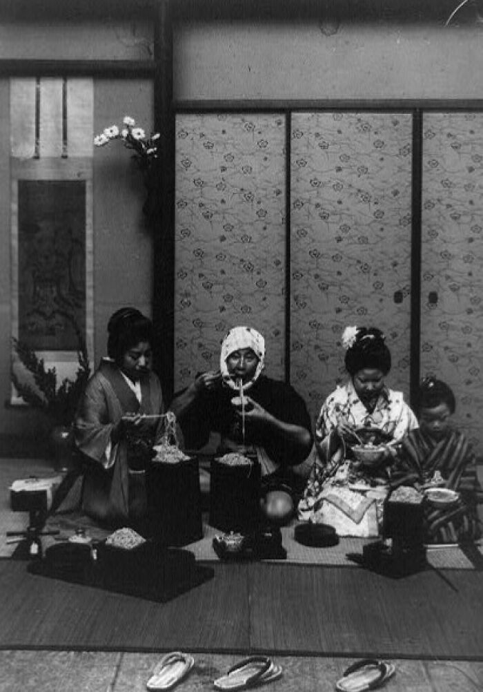 Black and white photo of a Japanese family eating noodles indoors, depicting daily life in Japan in the 1800s.